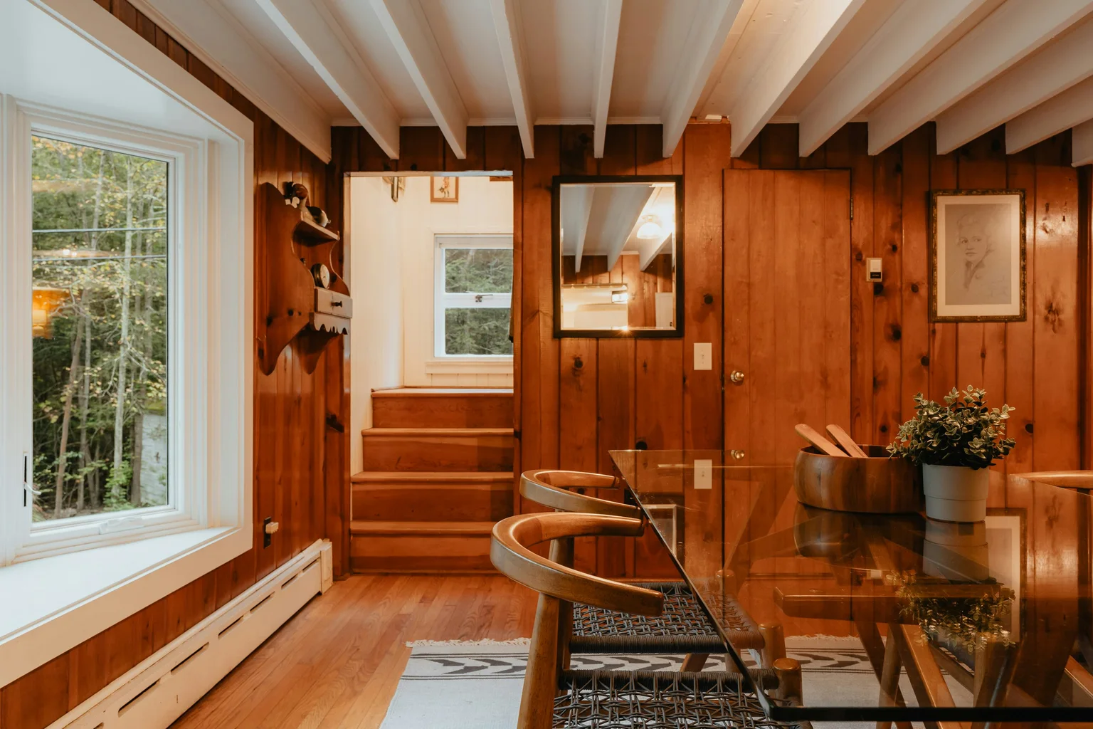 Wood-paneled dining room with a glass table and white ceiling beams